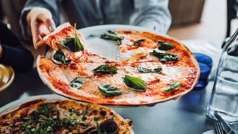 Close up of young Asian woman getting a slice of freshly made pizza. Enjoying her meal in an outdoor restaurant. Italian cuisine and culture. Eating out lifestyle