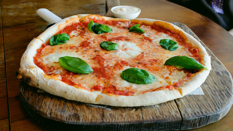 Circle Pizza Margarita with mozzarella and basil leaves on a wooden stand or cutting board, on the table in a cafe or fast food restaurant. Traditional Italian cuisine. Vegetarian food.
