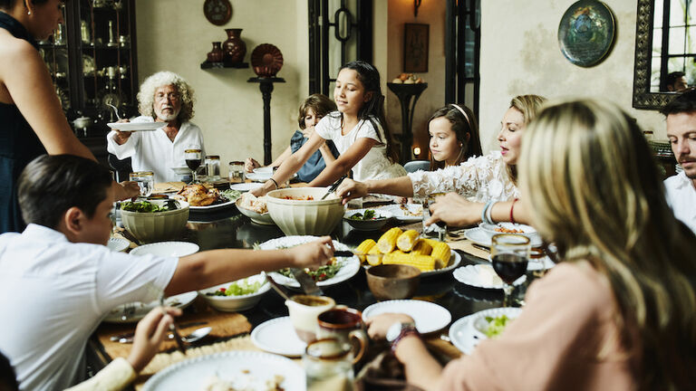 Young girl bringing platter of bread to dining room table during family celebration meal