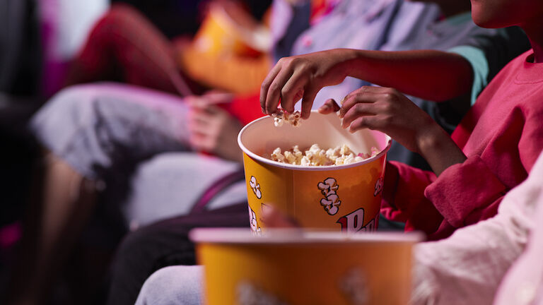 Midsection of friends sharing popcorn while sitting in theater