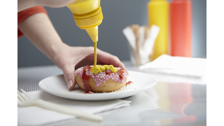 Woman squirting donut with ketchup and mustard