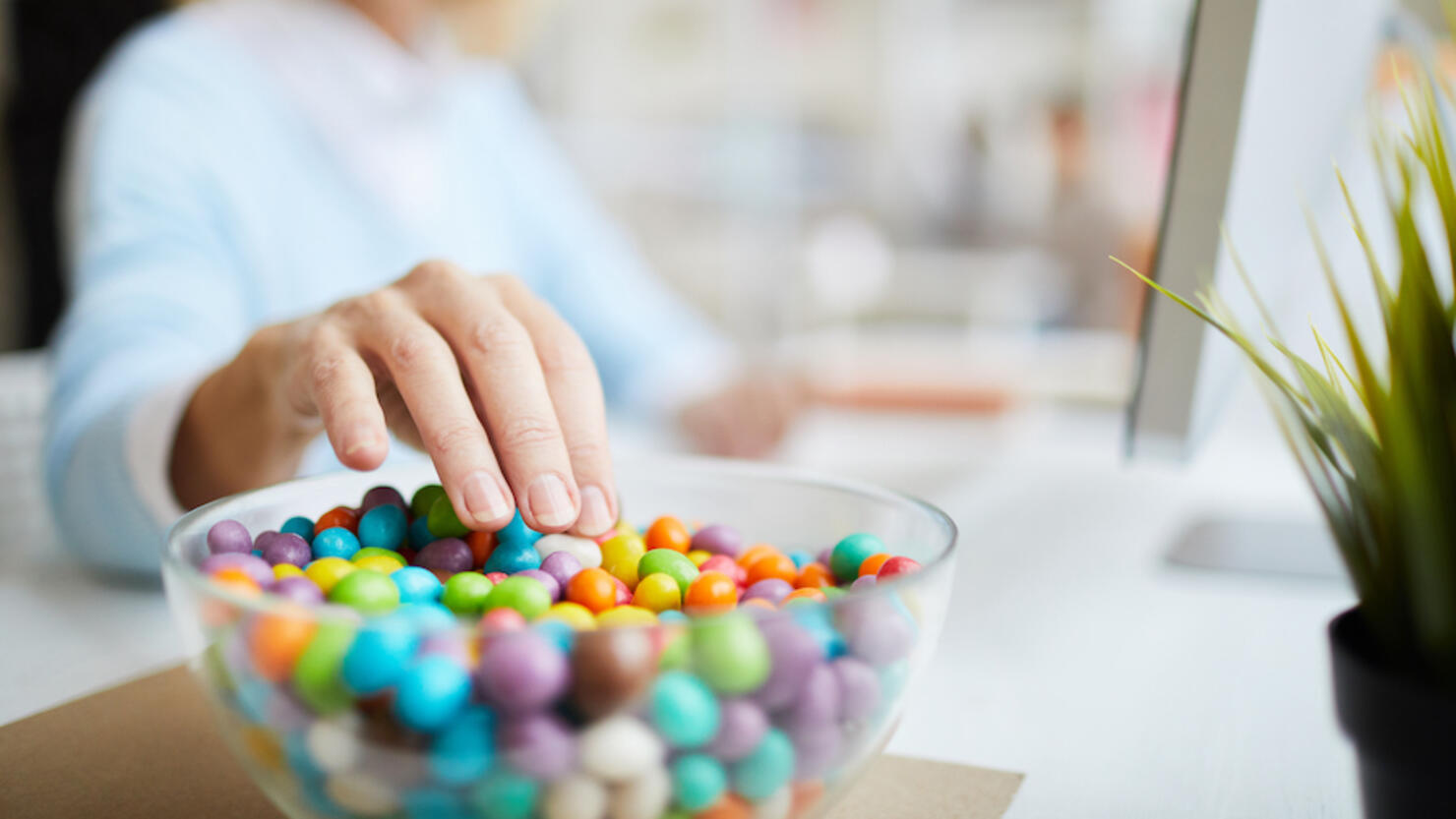 Close-up of unrecognizable businesswoman sitting at table and eating sweet beans while working in office