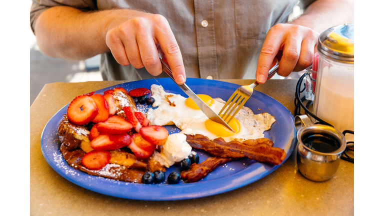 Man eating breakfast with sunny side up eggs, bacon, french toast and fresh fruits