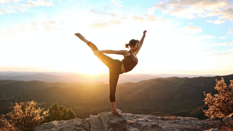 Woman Balancing On Rock At Mountain Against Sky During Sunset