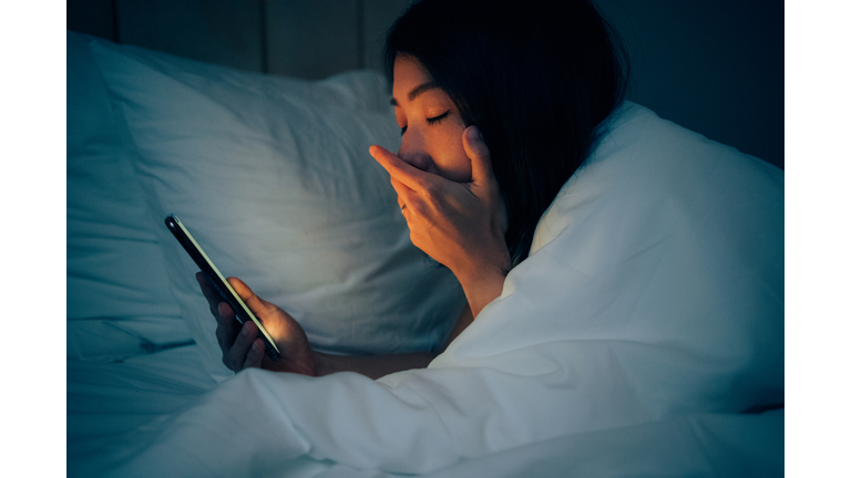 Woman hiding under the blanketed and using smart phone at late night on bed