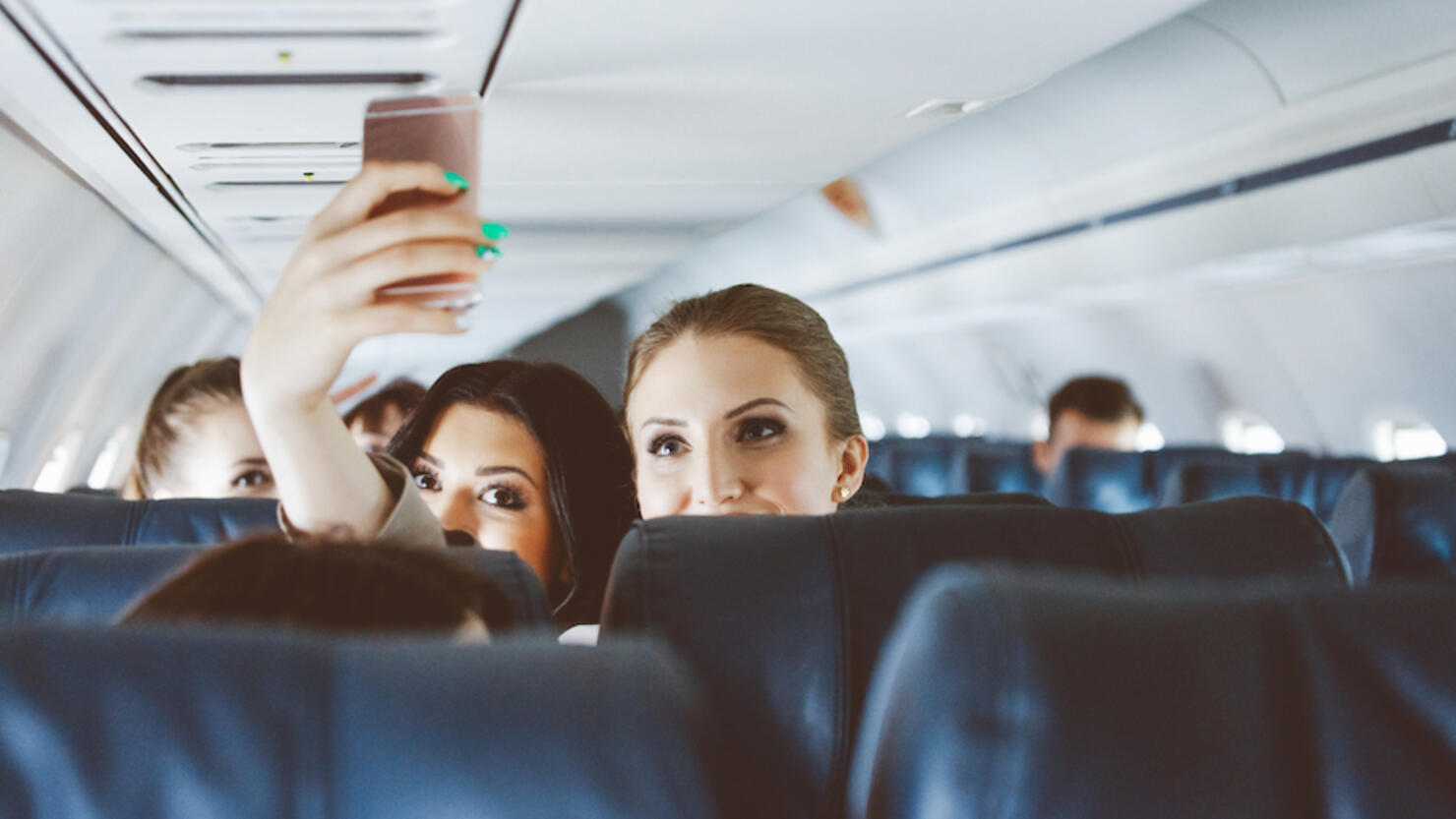 Young women taking selfie using smart phone during flight