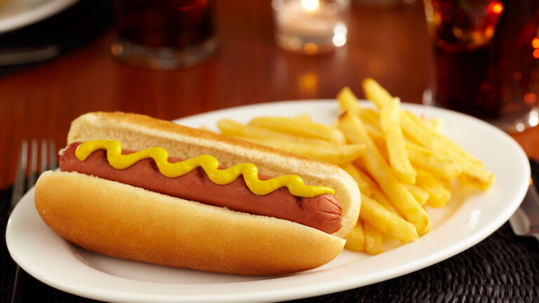 Hotdog with mustard and French fries on white platter