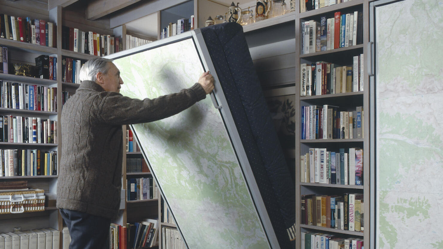 Senior man pulling Murphy bed in library of a traditional house