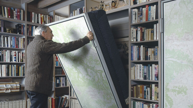 Senior man pulling Murphy bed in library of a traditional house