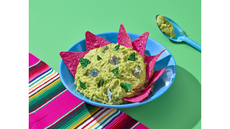 A guacamole pewter bowl with pink nachos. Shot over a green background and a sarape.