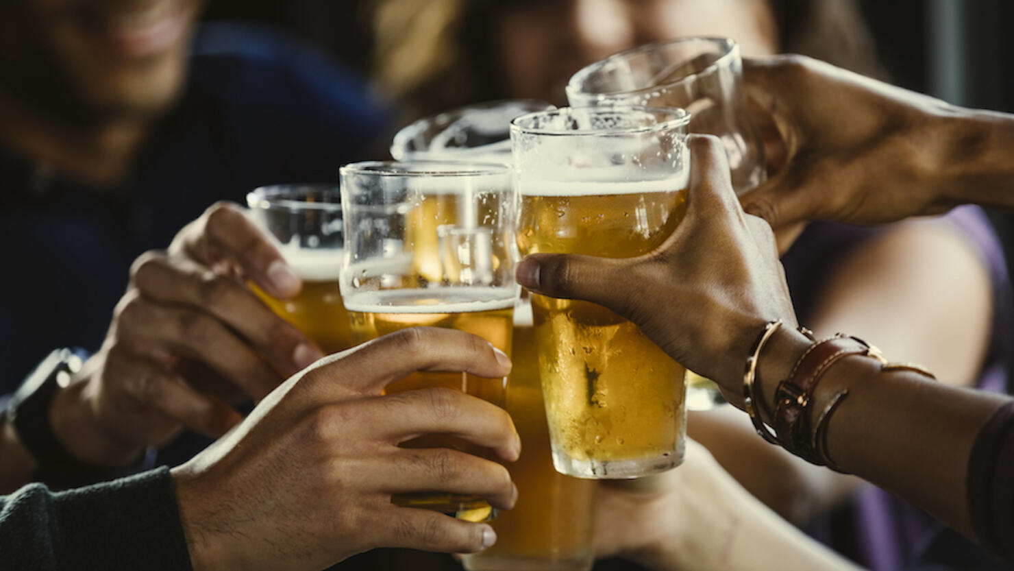 Group of friends toasting beer glasses at table in bar