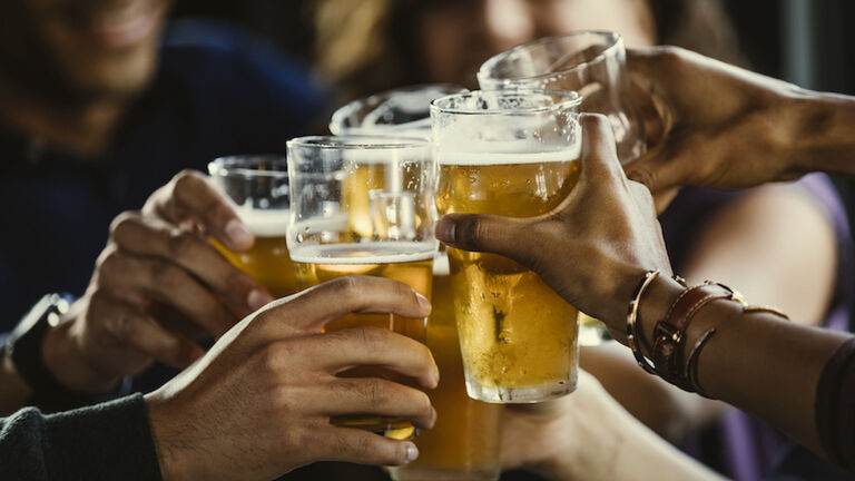Group of friends toasting beer glasses at table in bar