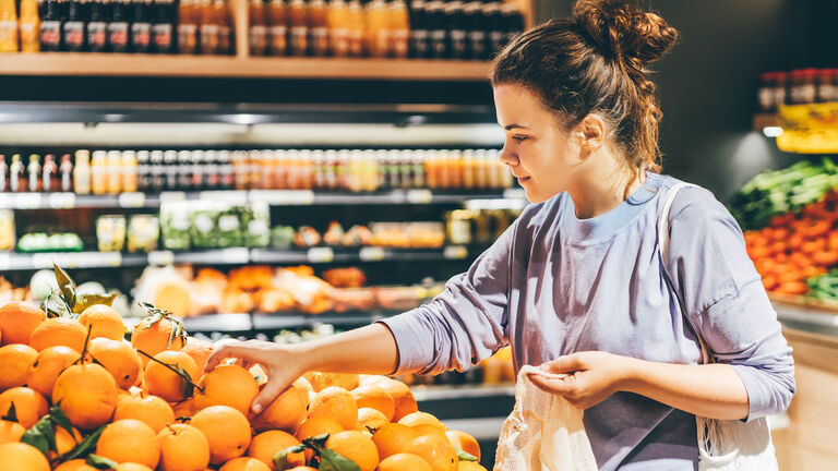 Woman choosing orange at market and using reusable eco bag.