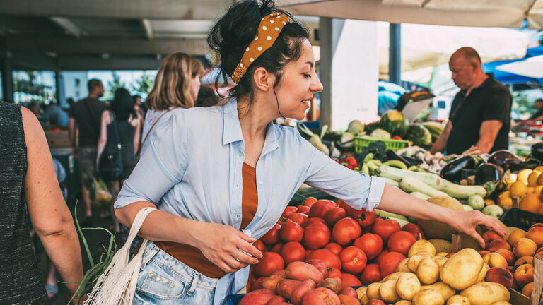 A young woman buys vegetables and fruits at the market .