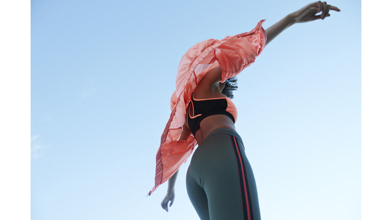 Fashionable woman wearing jacket with sports clothing against clear sky