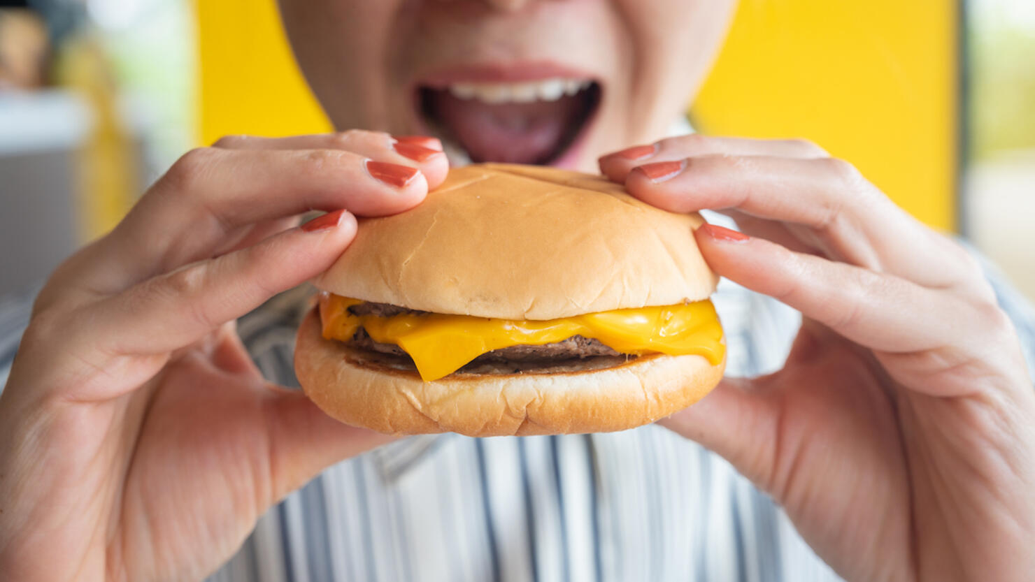 Close up of woman opened her mouth to eat a cheese burger.