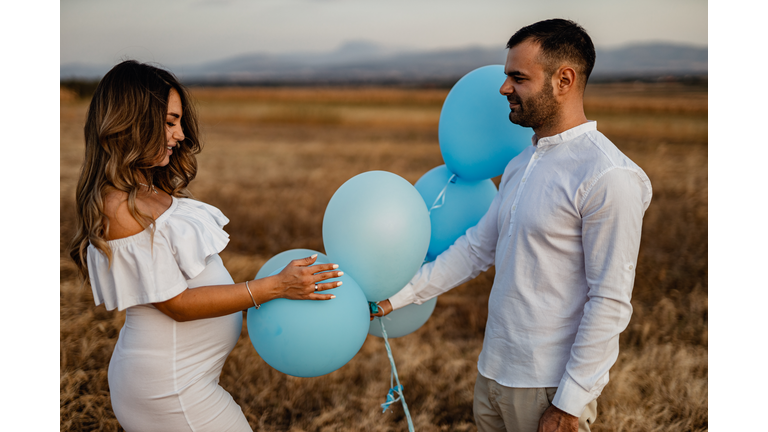 Young pregnant woman and young man with blue balloons in nature