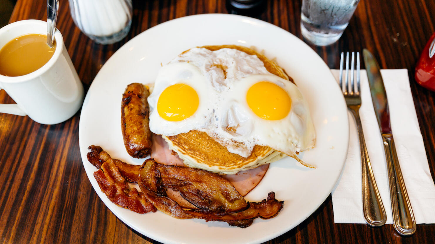 Traditional American breakfast with pancakes, fried eggs, bacon, sausage and ham served in a diner