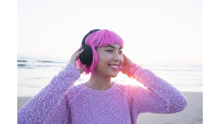 Young woman with pink hair listening to music on headphones