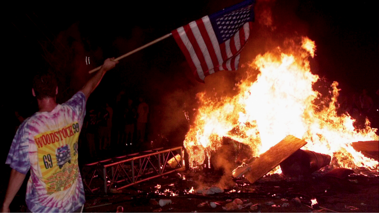 Man in front of fire holding flag