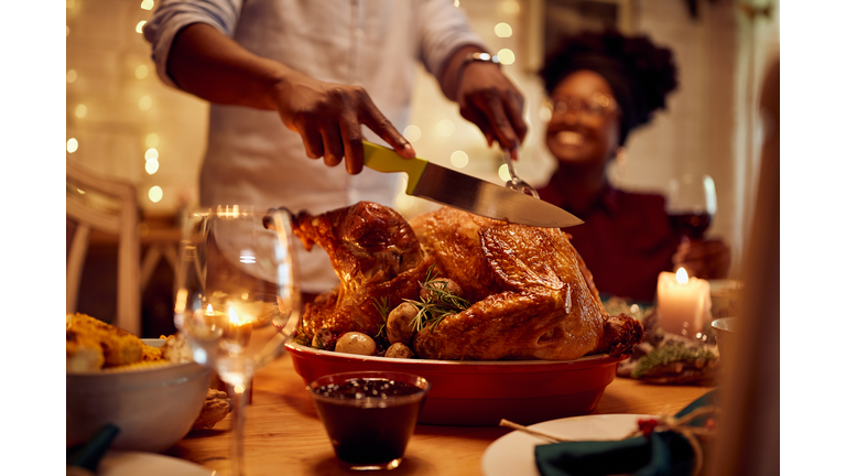 Close-up of African American man carving roasted Thanksgiving turkey.