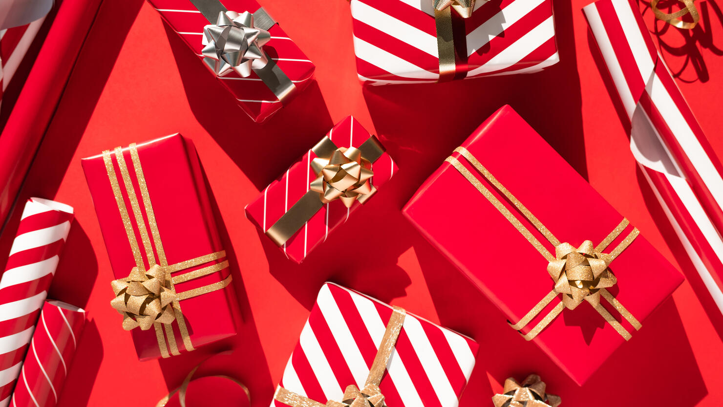 Set of many white-red gift boxes, ribbon, bows and wrapping paper on red table. Flat lay style