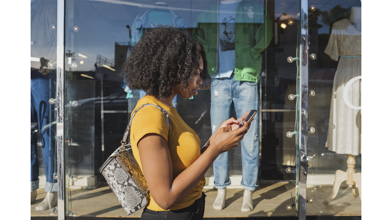 Young woman looking at phone outside shop window