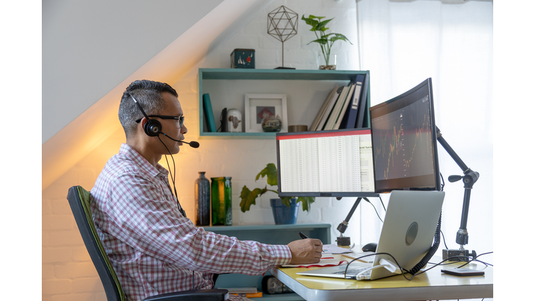 Man looking at currency trading app on his smart phone from his home office