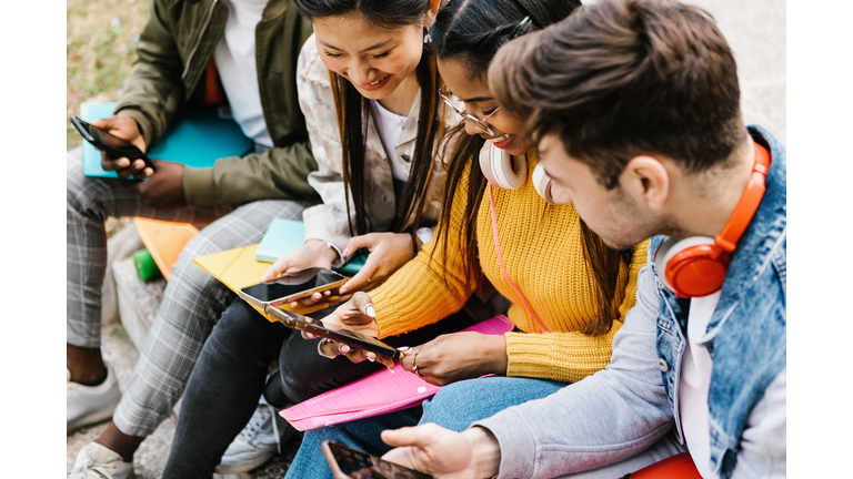 Diverse young teenage students having fun using mobile phone in college campus