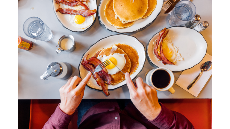 Man eating pancakes with bacon and eggs in a traditional American diner, personal perspective overhead view