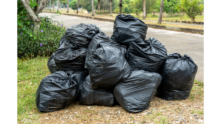 Black garbage bags on the road with green grass and plants background