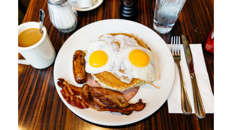 Traditional American breakfast with pancakes, fried eggs, bacon, sausage and ham served in a diner