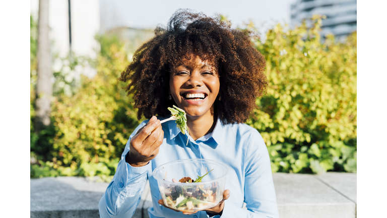 Happy businesswoman eating salad on sunny day