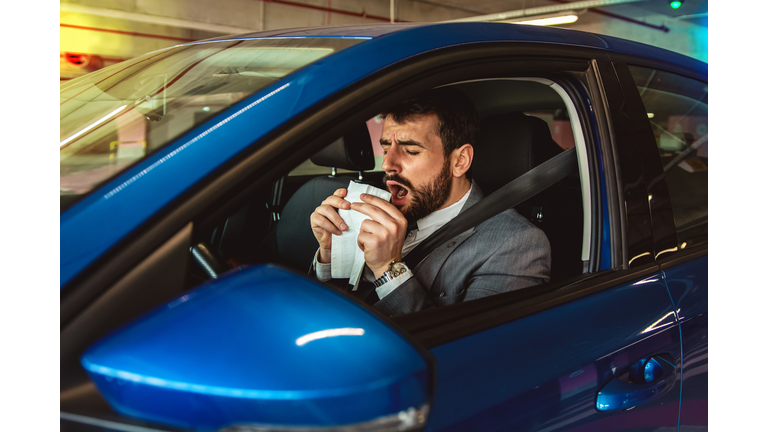 Businessman blowing his nose inside the car