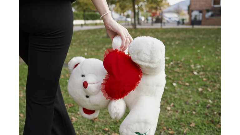 Close-up of woman walking and holding a white teddy bear with a red heart in the middle with the phrase I love you. Valentine concept