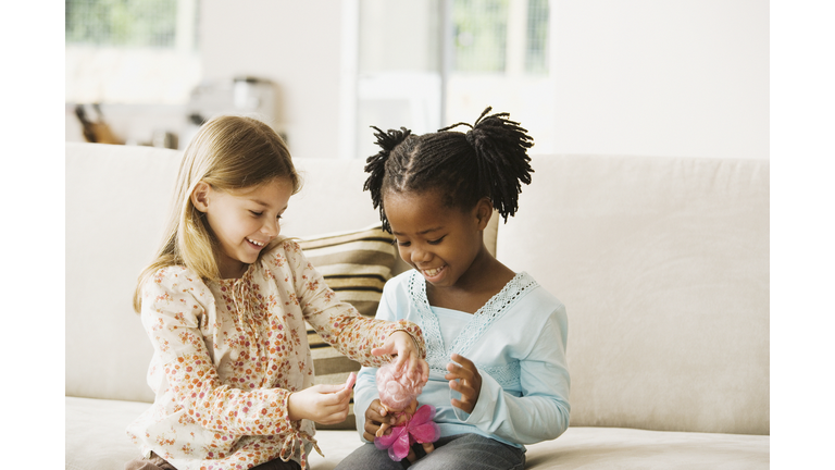 Two girls (4-6) playing with doll in living room, smiling
