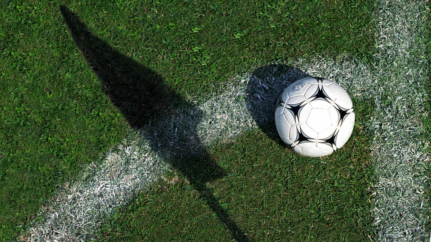 Football on grass by pitch marking and shadow of flag