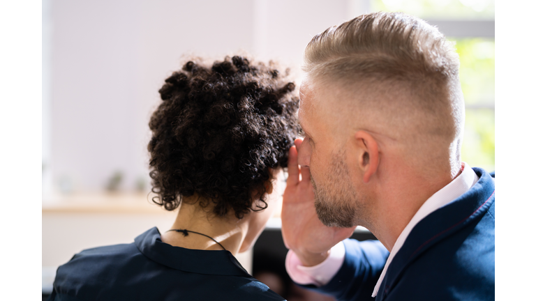 Businesswoman Whispering Into Male Partner's Ear