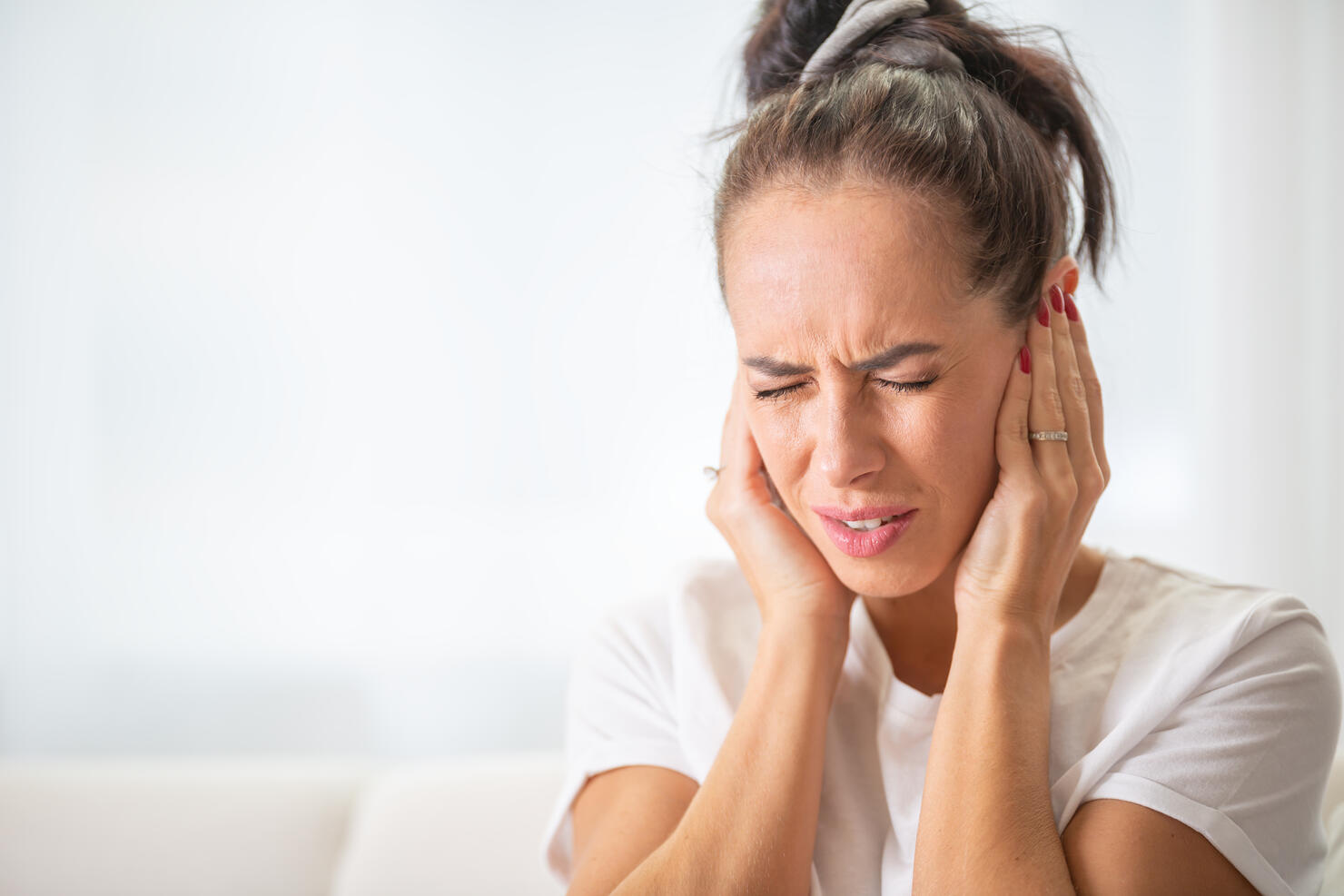 Woman closes hear ears with hands due to noise or ache in the ear or head frowning from the unpleasant experience.