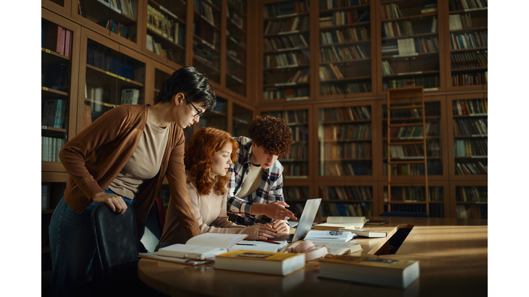 Group of high school students using laptop in library.