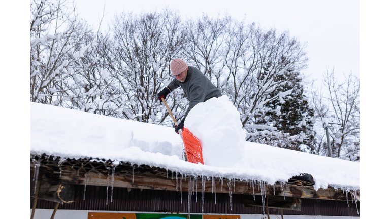 Senior man shoveling snow off roof