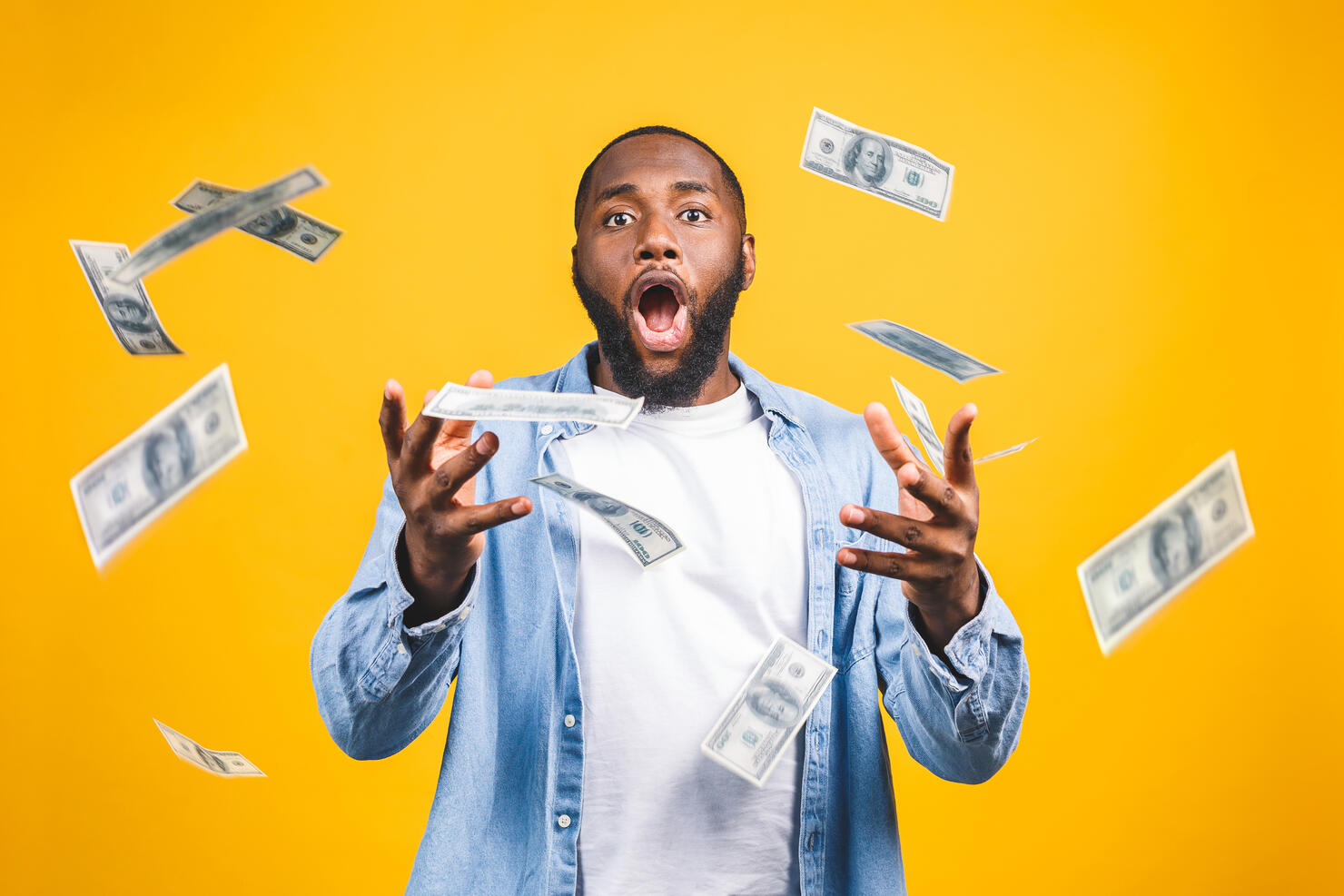 Portrait of a happy young afro american man throwing out money banknotes isolated over yellow background.