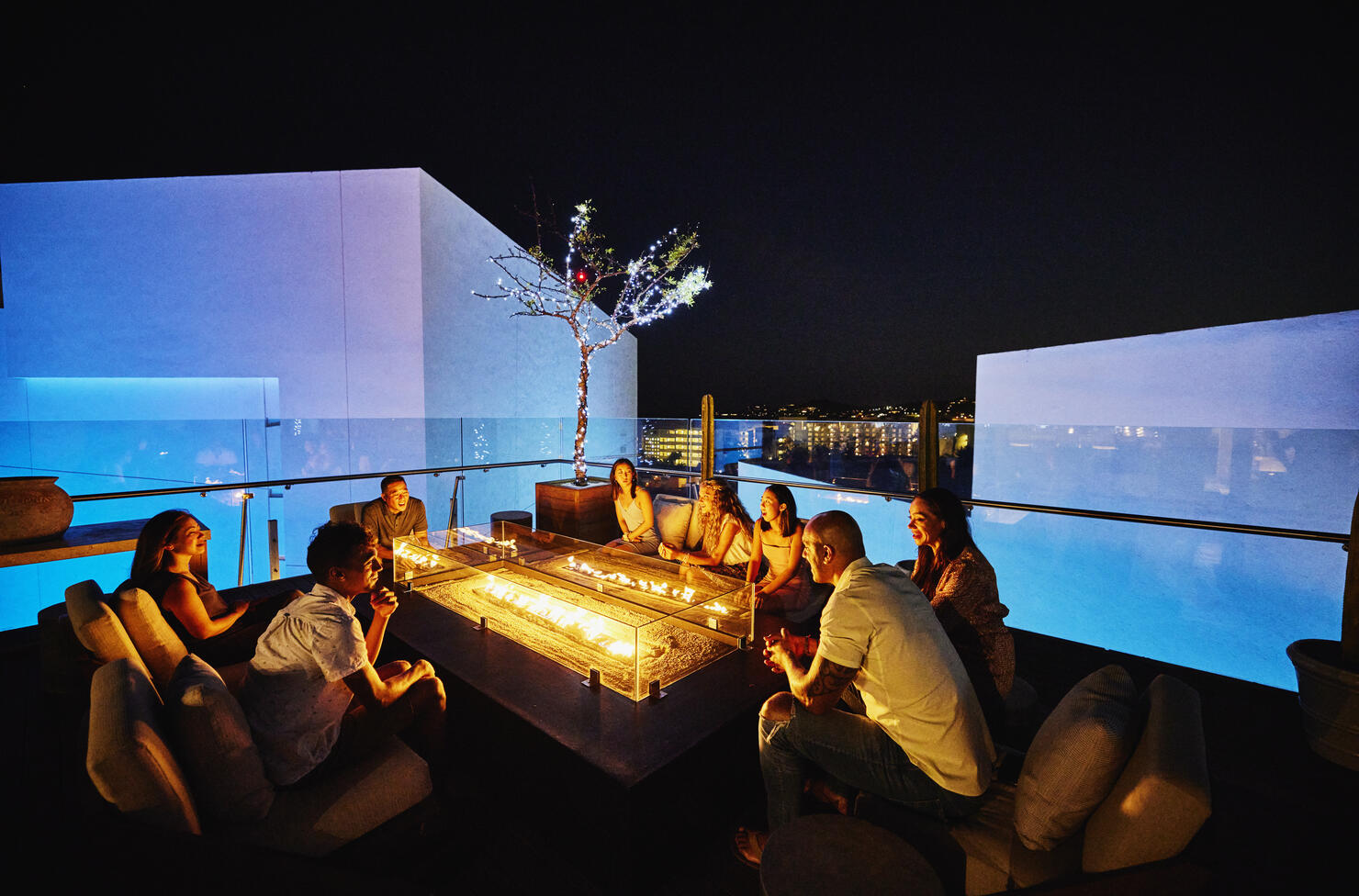 Wide shot of families relaxing around fire pit on rooftop at resort