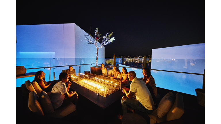 Wide shot of families relaxing around fire pit on rooftop at resort