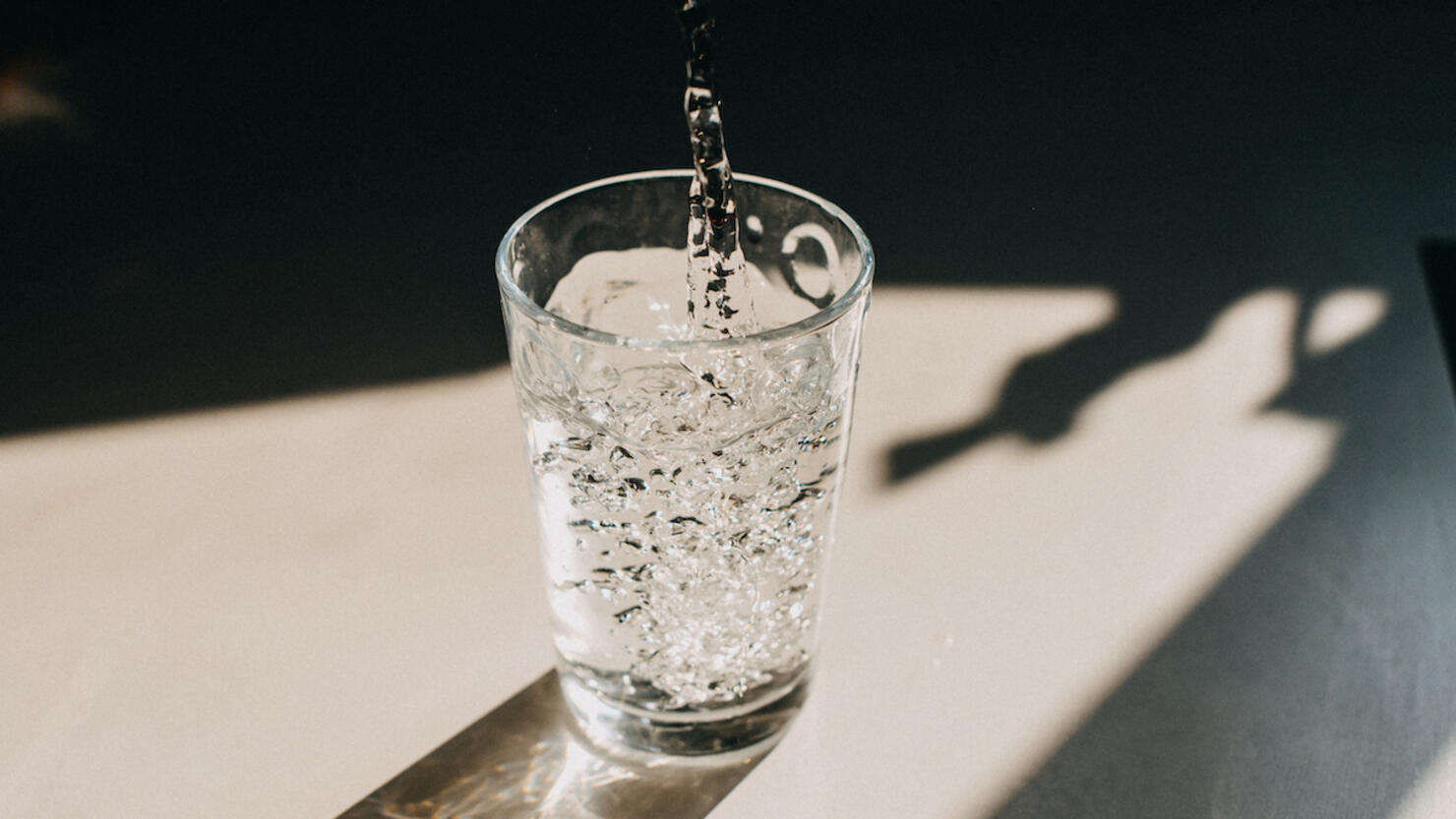 Water being poured in a glass of water that cast a beautiful shadow on a white kitchen countertop