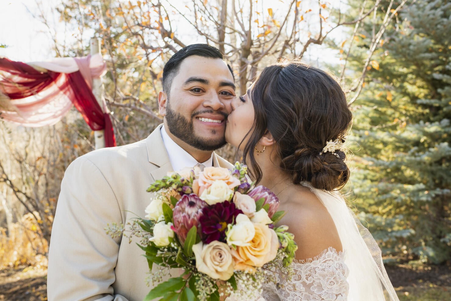 Bride kissing groom on cheek at outdoor wedding