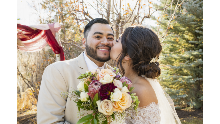 Bride kissing groom on cheek at outdoor wedding