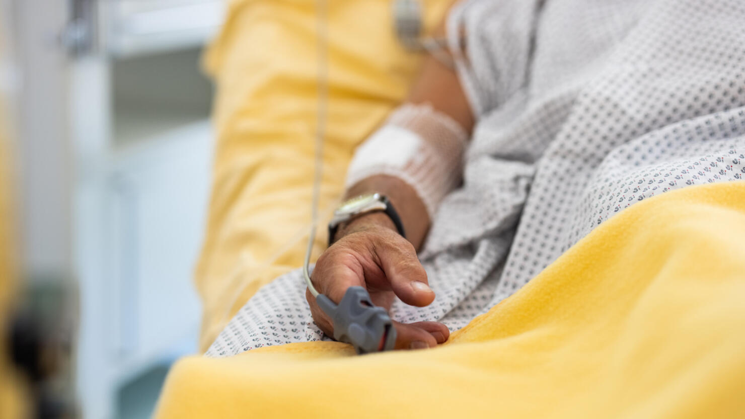 Close-up of a male patient's hand in a hospital bed with oximeter