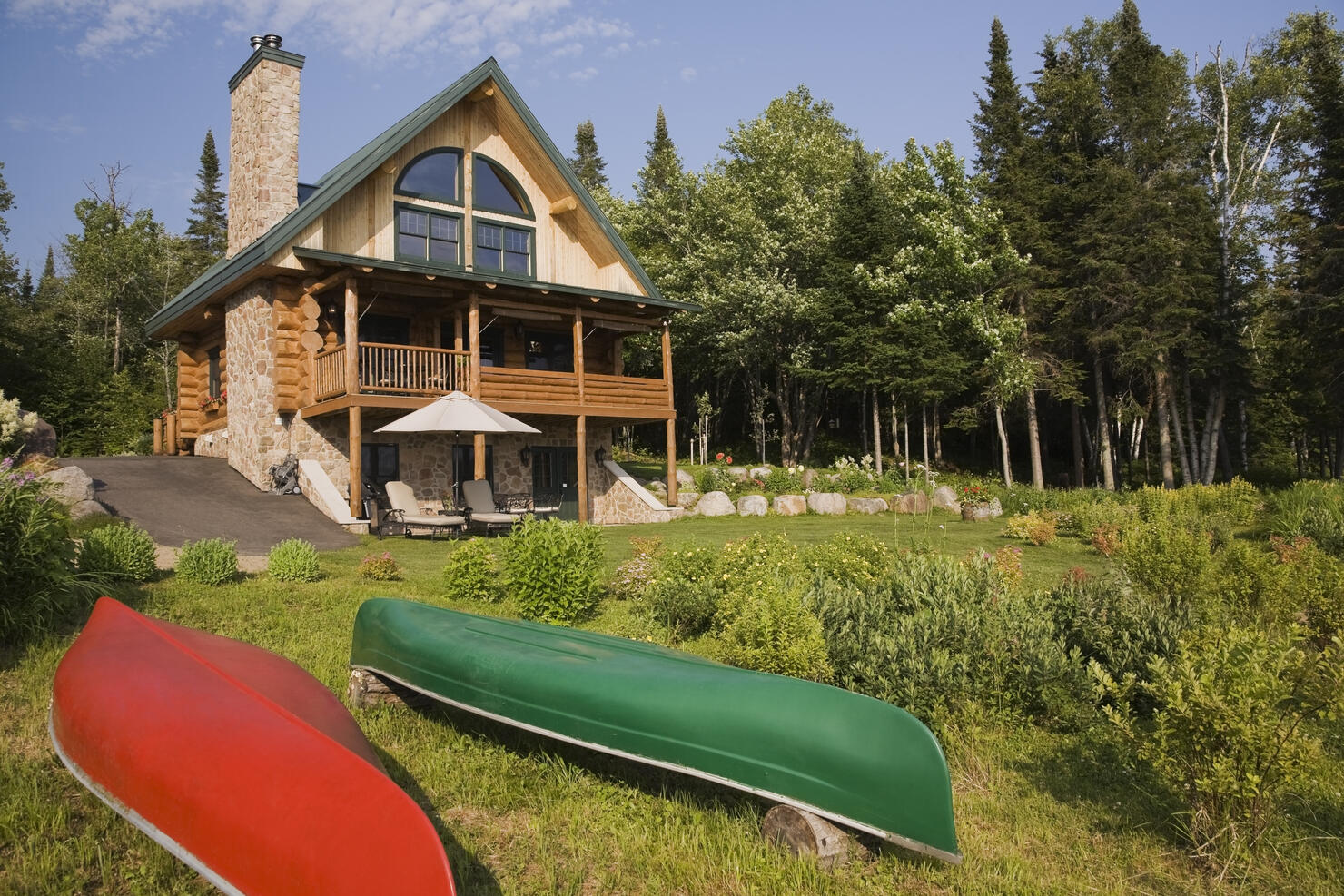 Handcrafted spruce log home with fieldstone chimney and green metal roof in summer, Quebec, Canada