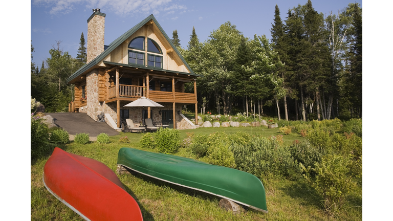 Handcrafted spruce log home with fieldstone chimney and green metal roof in summer, Quebec, Canada